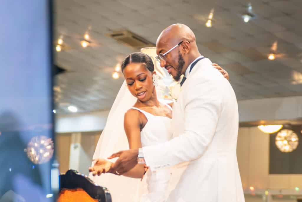 A bride and groom both wearing white sharing an intimate dance at their wedding reception, looking down smiling at their joined hands.